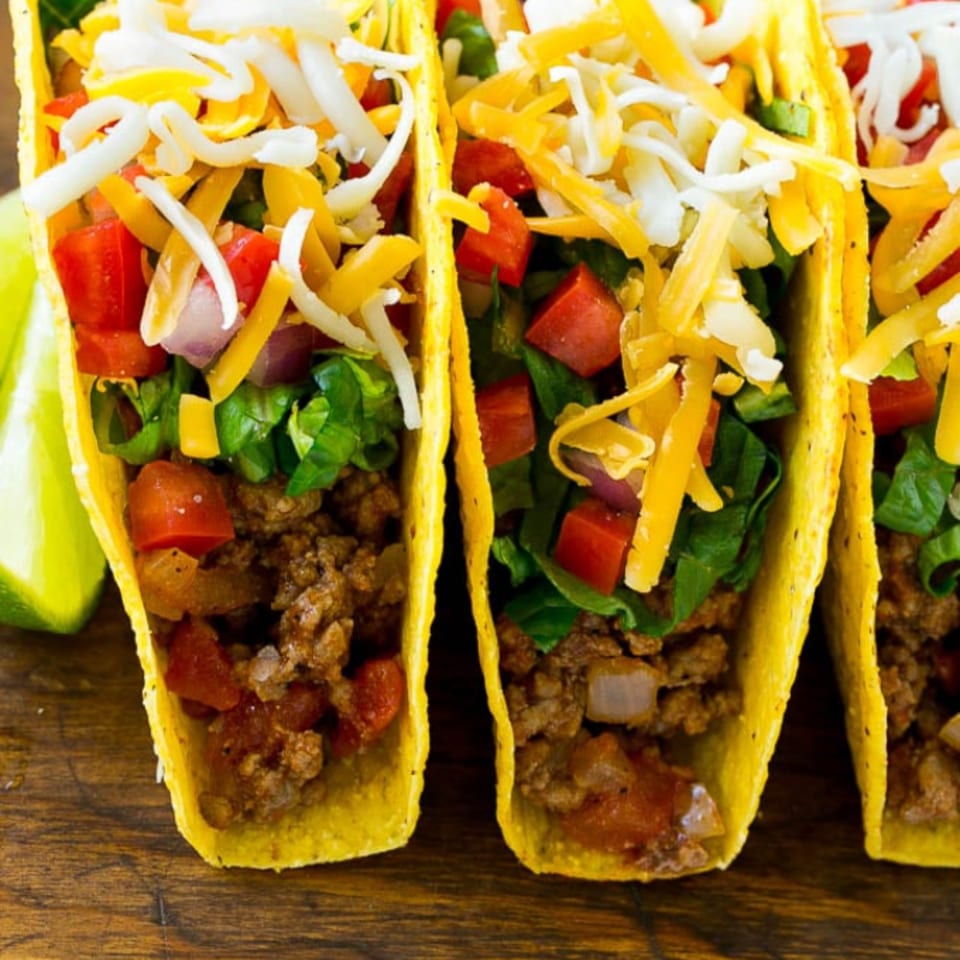 Three El Paso Mexican Grill tacos with seasoned ground beef, lettuce, tomatoes, and shredded cheese.
