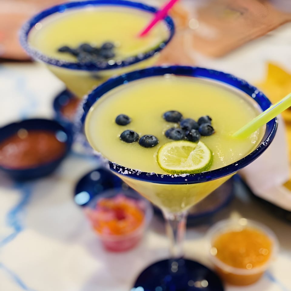 Two El Paso Mexican Grill margaritas with blueberries, lime, and salt rims, with salsa.