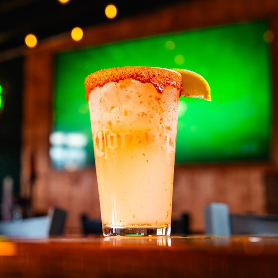 A Mexican cocktail with a chili-lime rim and lime wedge, on a bar with a green screen.