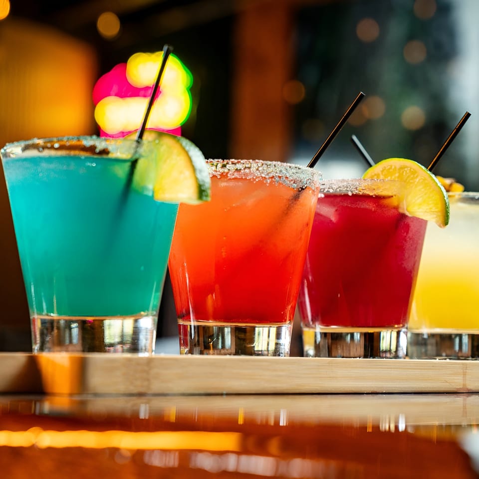 Four colorful margaritas, garnished with lime and salt, on a wooden tray at El Paso Mexican Grill.