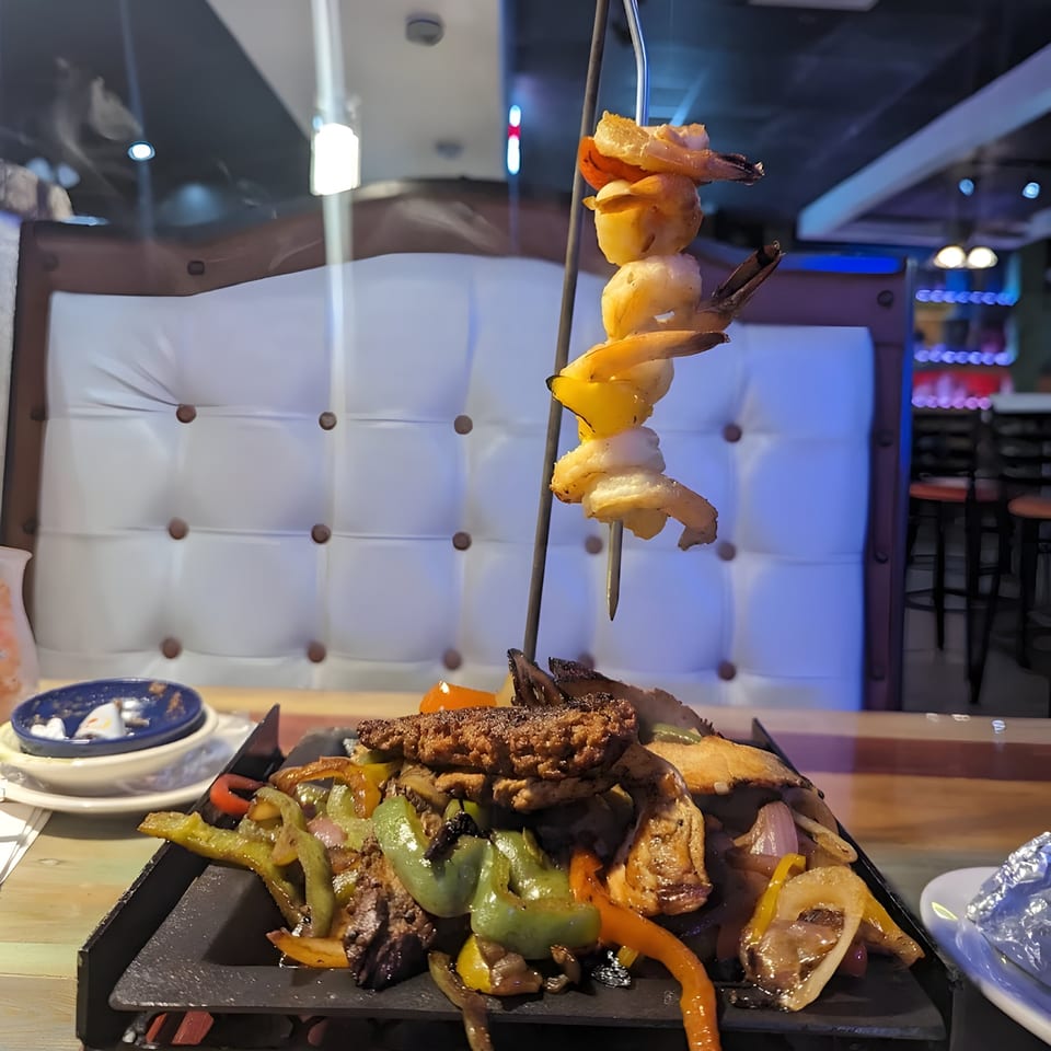 Sizzling El Paso Mexican Grill fajitas with shrimp, steak, chicken, and vegetables on a hot plate.